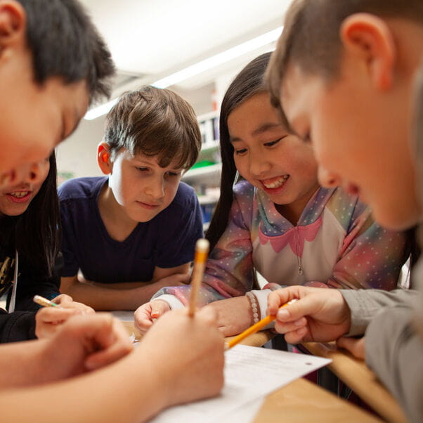 A group of young children at school sitting around a table together working on a project.