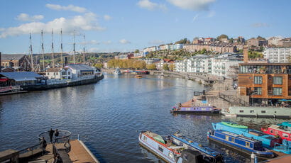 Panoramic view of Bristol harbour' with coloured houses on the hill and boats/ships on the waterfront.
