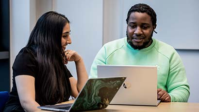Couple of students sat together looking at laptops.