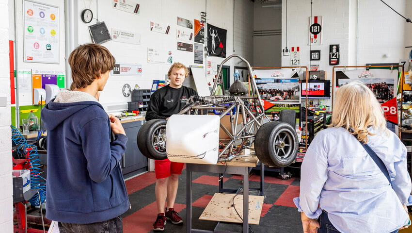 A prospective student and they're family being shown a demo of a racing car in the manufacturing workshop.