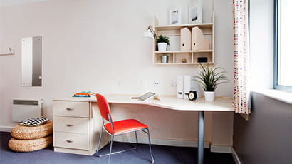 A desk and red chair in a student room with natural light coming in through the window.
