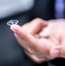 A close up of a hand with a contact lens on their index finger.
