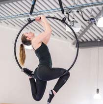 Student in air performing trick on an aerial hoop.