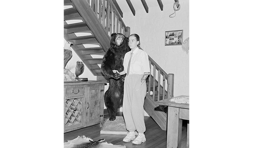 A woman stands in front of a staircase next to a taxidermy bear