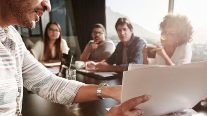 Group of people sat around a table discussing a document at a meeting.