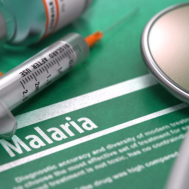 The word Malaria on a green background with blurred text and composition of pills, syringe and stethoscope. 