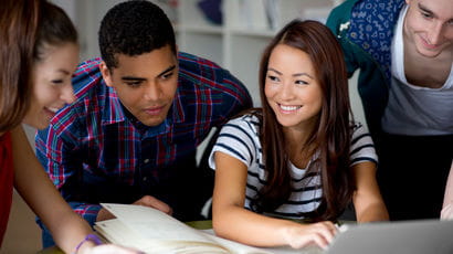 Four students happily looking at a laptop together.