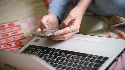 Hands holding a mobile phone in front of a laptop.
